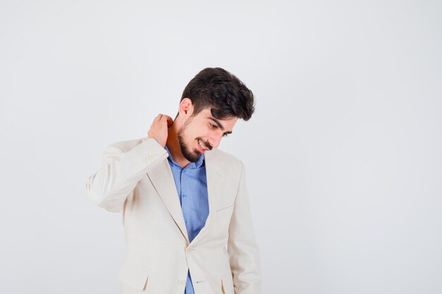 Hombre joven rascándose el cuello con camisa azul y chaqueta de traje blanco y mirando feliz