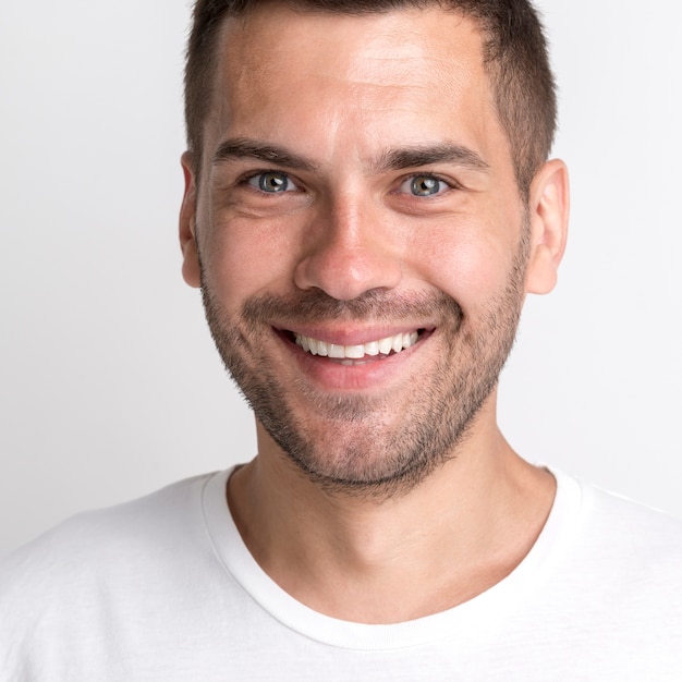 Hombre joven de rastrojo sonriente en camiseta blanca contra la pared lisa