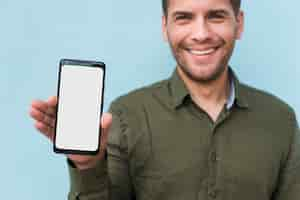 Foto gratuita hombre joven rastrojo sonriente sosteniendo blanco smartphone de pantalla en blanco