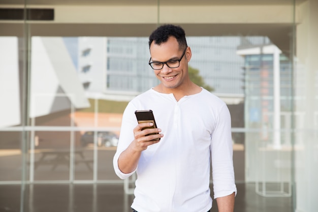 Hombre joven de la raza mixta que manda un SMS en el teléfono, sonriendo. Vista frontal