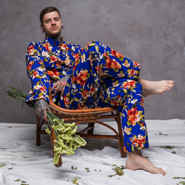 Hombre joven relajado triste que se sienta en la silla que sostiene la flor del limonium disponible