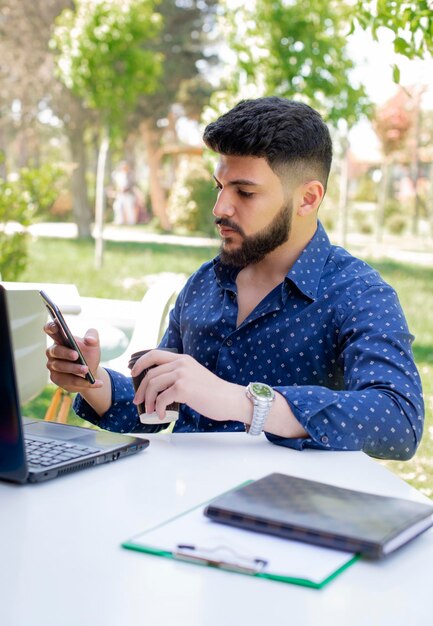 Hombre joven con reloj de moda con teléfono celular para llamar mientras está sentado en la mesa