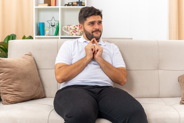 Hombre joven en ropa casual cogidos de la mano juntos esperando sorpresa sentado en un sofá en la sala de luz