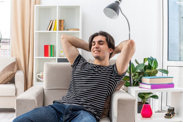 Hombre joven en ropa casual feliz y positivo relajante pasar el fin de semana sentado en la silla en la sala de luz