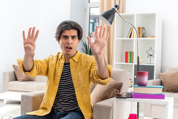 Hombre joven en ropa casual mirando sorprendido mostrando el número nueve con los dedos sentado en la silla en la sala de luz