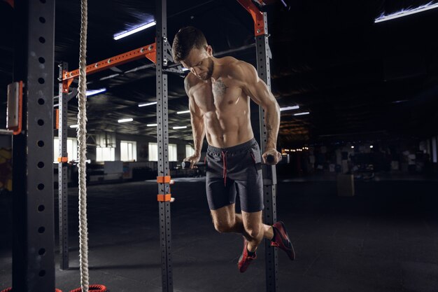 Hombre joven sano, atleta haciendo ejercicios, dominadas en el gimnasio. Modelo masculino soltero practicando duro y entrenando la parte superior del cuerpo. Concepto de estilo de vida saludable, deporte, fitness, culturismo, bienestar.