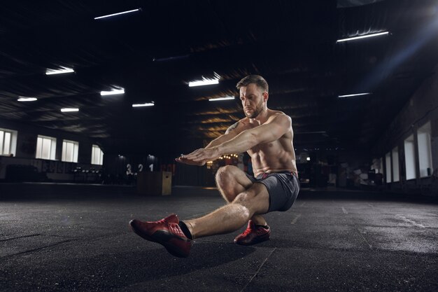 Hombre joven sano, atleta haciendo ejercicios de equilibrio, sentadillas en el gimnasio. Modelo único practicando duro, entrenando la parte inferior del cuerpo. Concepto de estilo de vida saludable, deporte, fitness, culturismo, bienestar.