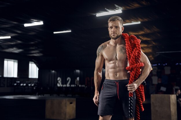 Hombre joven sano, atleta posando confiado con las cuerdas en el gimnasio.