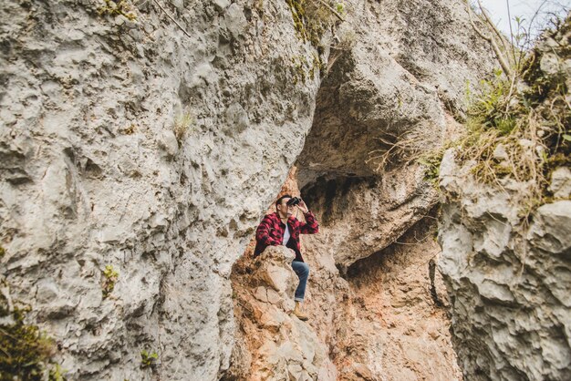 Hombre joven sentado en una roca y usando sus prismáticos