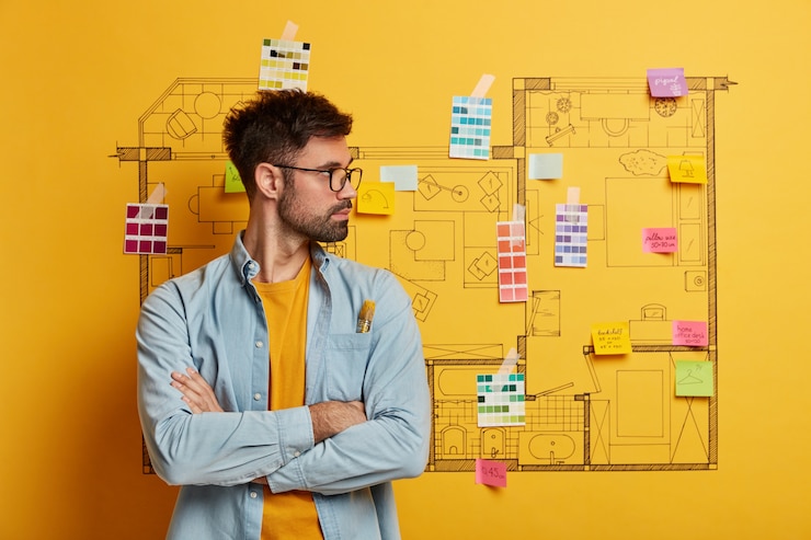 Foto gratuito un hombre joven y serio se encuentra al lado del boceto de diseño de la casa listo para la renovación