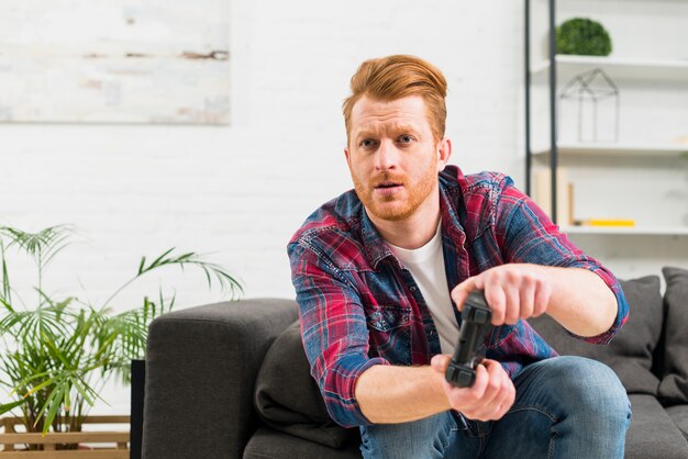 Hombre joven serio que juega el videojuego en casa