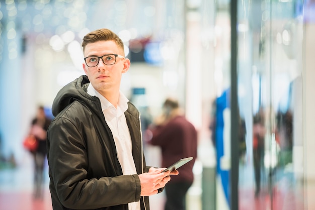 Hombre joven serio que sostiene la tableta digital en la mano que mira lejos