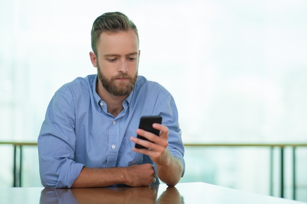 Hombre joven serio que usa smartphone en el vector del café