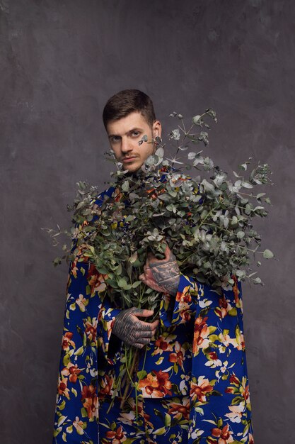 Hombre joven serio con el tatuaje en su mano que sostiene ramas de la planta