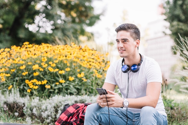 Hombre joven con smartphone sentado en el parque