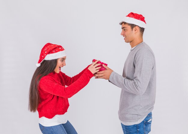 Hombre joven en sombrero de Navidad con caja actual cerca de mujer asombrada