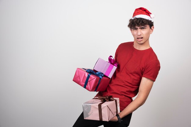 Hombre joven con sombrero de Santa con regalos pesados.