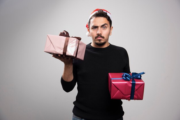 Un hombre joven con un sombrero de Santa sosteniendo los regalos de Año Nuevo.