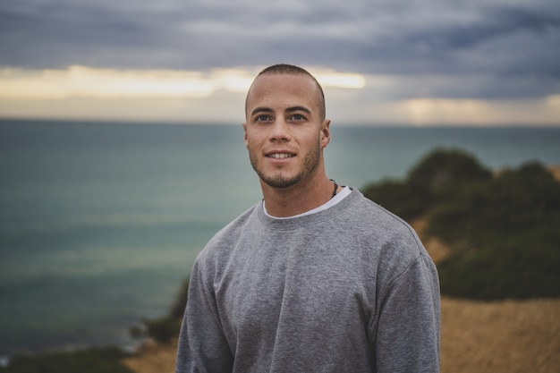 Hombre joven sonriendo y de pie sobre un acantilado cerca del hermoso mar