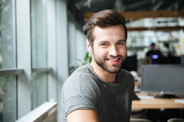 Hombre joven sonriente hermoso que se sienta en coworking de la oficina