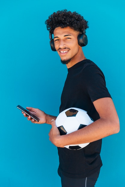 Foto gratuita hombre joven sonriente que se coloca con fútbol y el teléfono