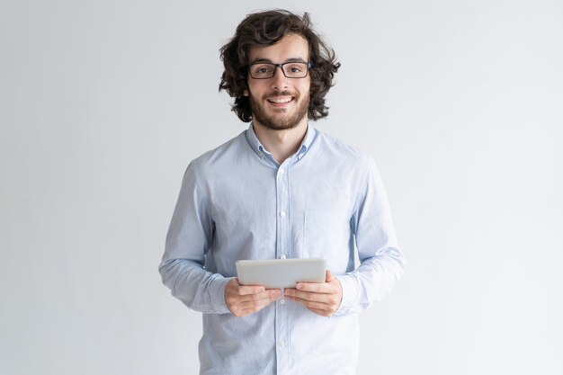 Hombre joven sonriente que coloca y que sostiene la tableta