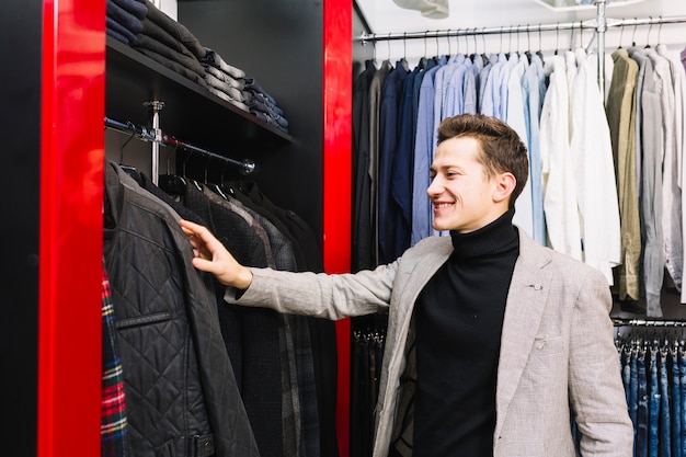 Hombre joven sonriente que comprueba la ropa en el estante