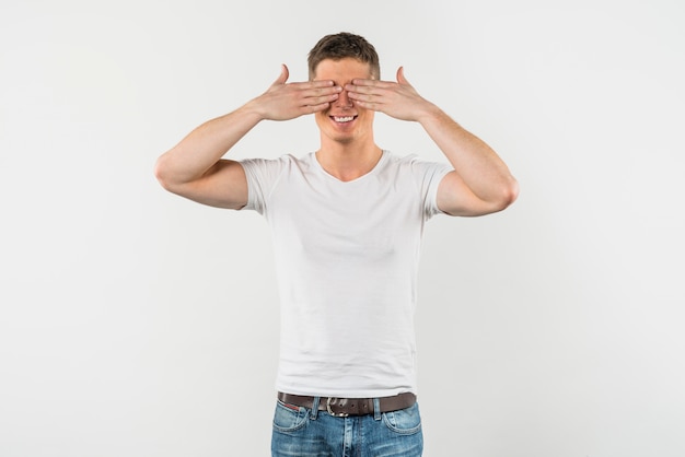 Foto gratuita hombre joven sonriente que cubre sus ojos aislados en el fondo blanco