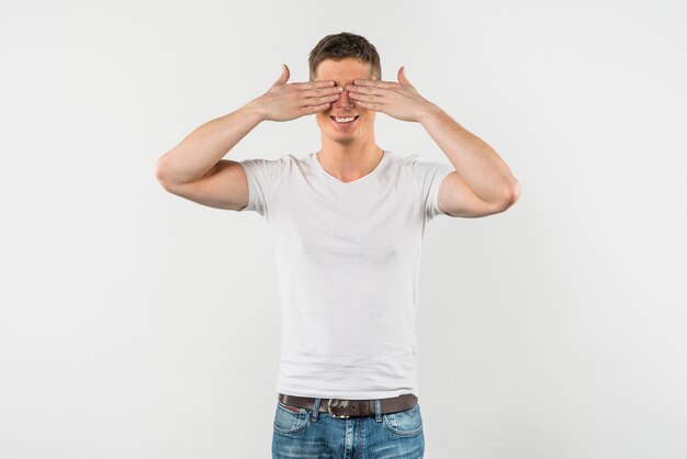 Hombre joven sonriente que cubre sus ojos aislados en el fondo blanco