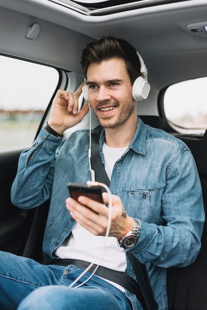 Hombre joven sonriente que disfruta de la música en el auricular asociado al teléfono móvil