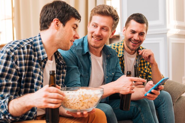 Hombre joven sonriente que muestra algo en el teléfono móvil a su amigo