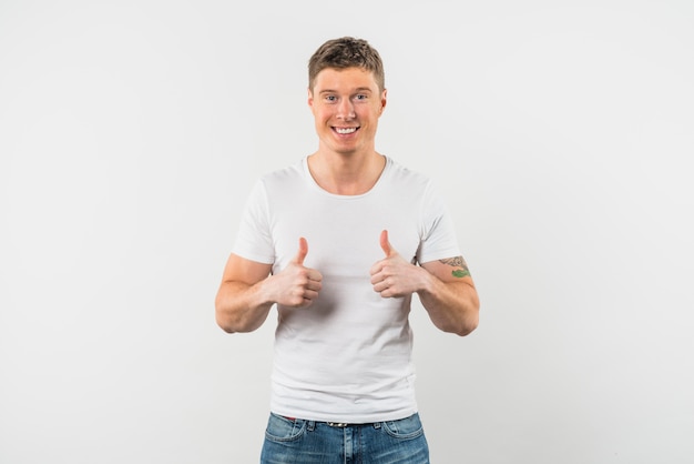 Hombre joven sonriente que muestra el pulgar para arriba con dos manos contra el fondo blanco