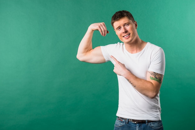 Foto gratuita hombre joven sonriente que muestra su músculo muscular contra fondo verde