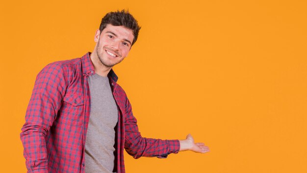 Hombre joven sonriente que presenta algo en un fondo anaranjado