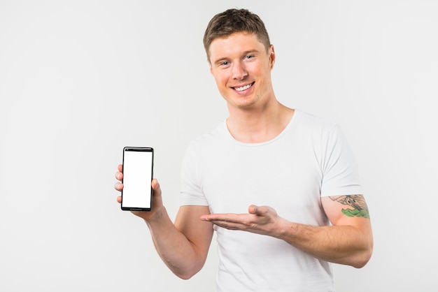 Hombre joven sonriente que presenta este nuevo teléfono inteligente con pantalla blanca