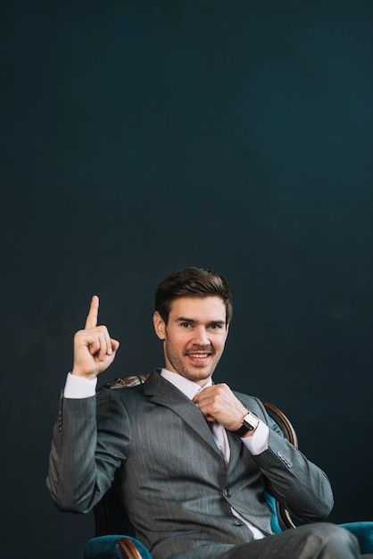 Hombre joven sonriente que señala el dedo hacia arriba contra fondo negro