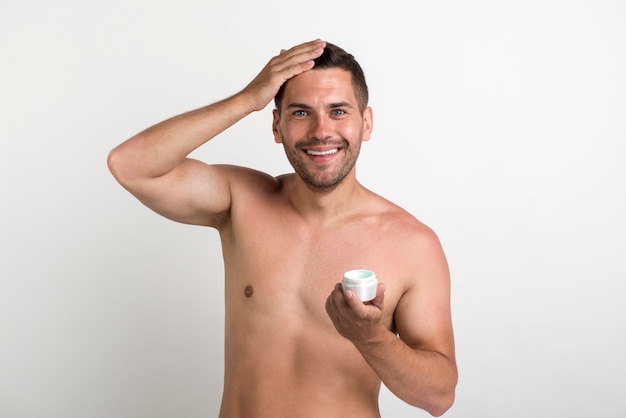 Hombre joven sonriente que sostiene el envase de la crema del pelo y que mira la cámara