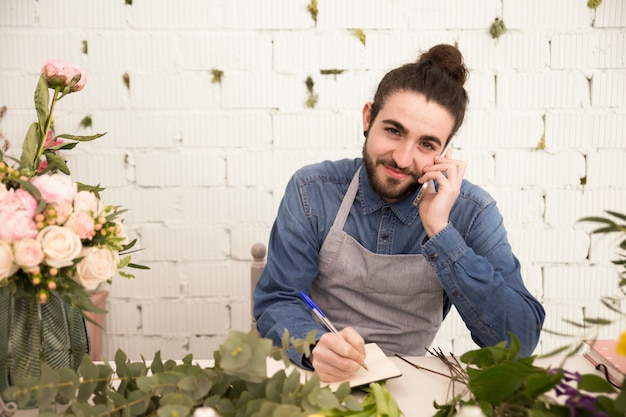 Hombre joven sonriente que toma orden en el teléfono móvil en la floristería