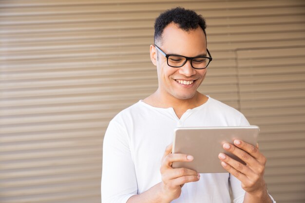 Hombre joven sonriente de la raza mixta que trabaja en la tableta. Vista frontal