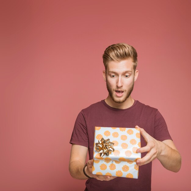 Hombre joven sorprendido que abre la caja de regalo floral con el arco de oro