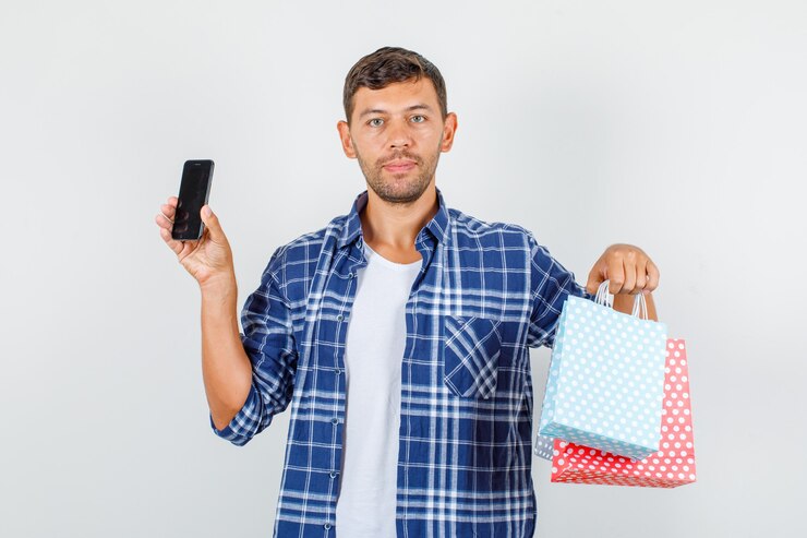 Foto gratuito hombre joven sosteniendo bolsas de papel y smartphone en vista frontal de la camisa.