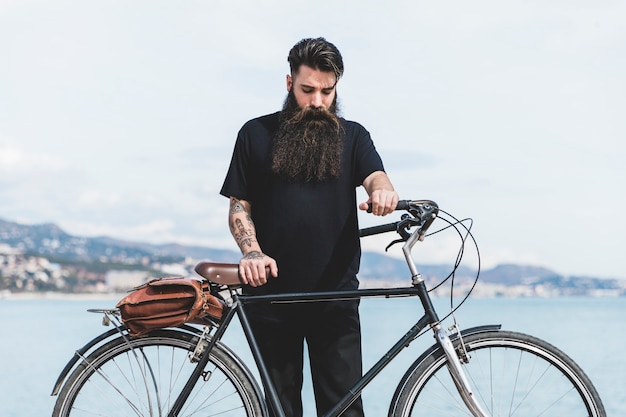 Foto gratuita hombre joven con su bicicleta de pie cerca de la costa
