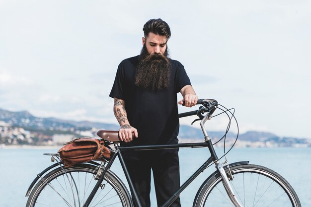 Hombre joven con su bicicleta de pie cerca de la costa