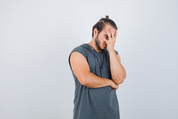 Hombre joven con sudadera con capucha inclinada cara a mano y con aspecto cansado, vista frontal.