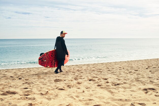 Hombre joven surfista en la playa con tabla de surf