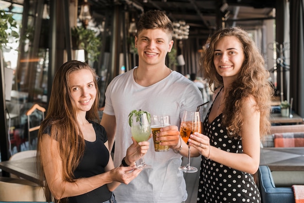 Hombre joven con sus dos amigas sosteniendo copas de bebidas