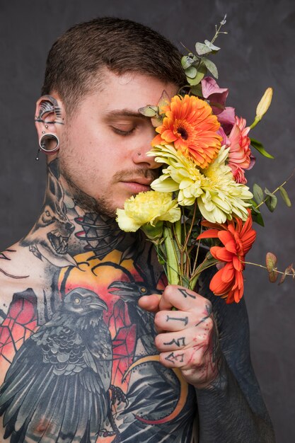 Hombre joven con tatuado en su cuerpo sosteniendo la flor en la mano