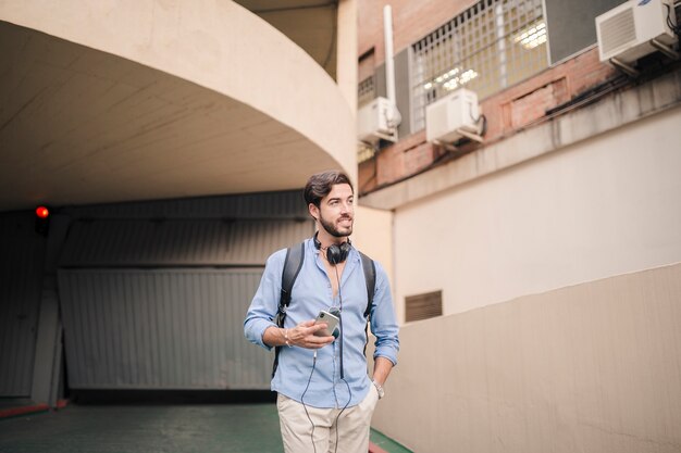 Hombre joven con teléfono inteligente de pie cerca del edificio