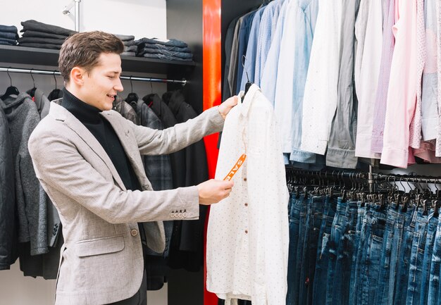 Hombre joven en la tienda que controla un precio en la camisa