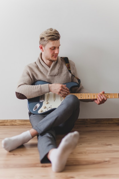 Hombre joven tocando la guitarra sentado en el suelo